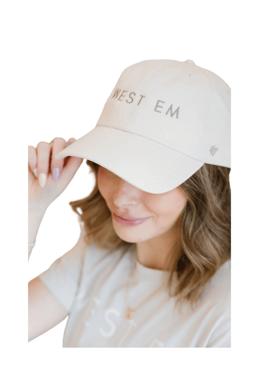 West Em ’47 Hat in tan modeled by Rae – stylish adjustable cap with embroidered logo at West Em Medical Spa