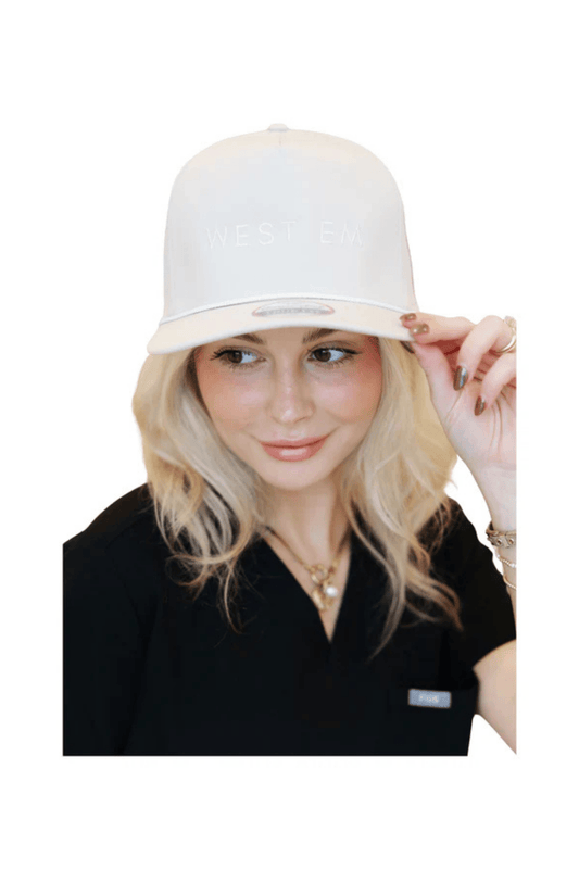 West Em tan trucker hat modeled by Rae – breathable mesh-back cap with embroidered logo at West Em Medical Spa